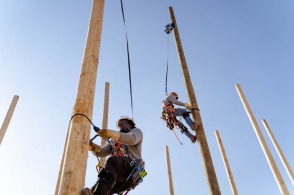 Two lineworkers practice down climbing on training poles attached to SafeLines