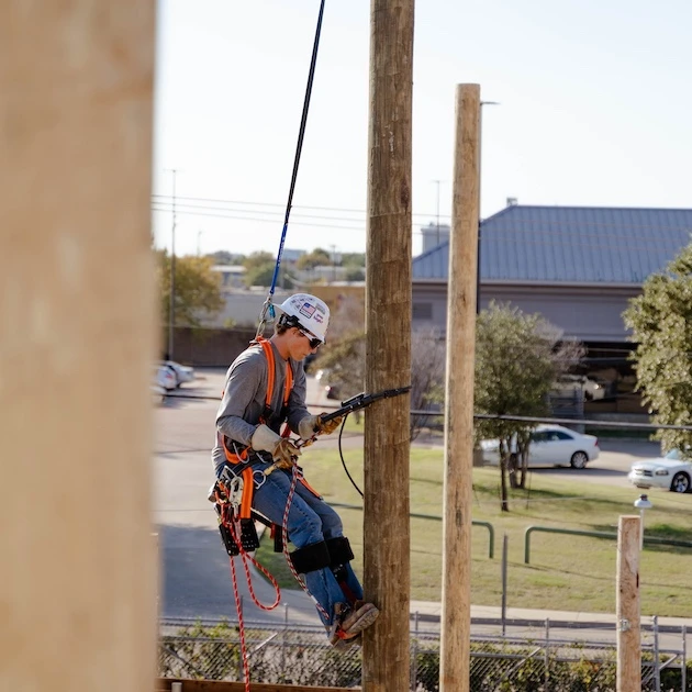 A lineworker climbing a pole using traditional methods, attached to TruBlue SafeLine